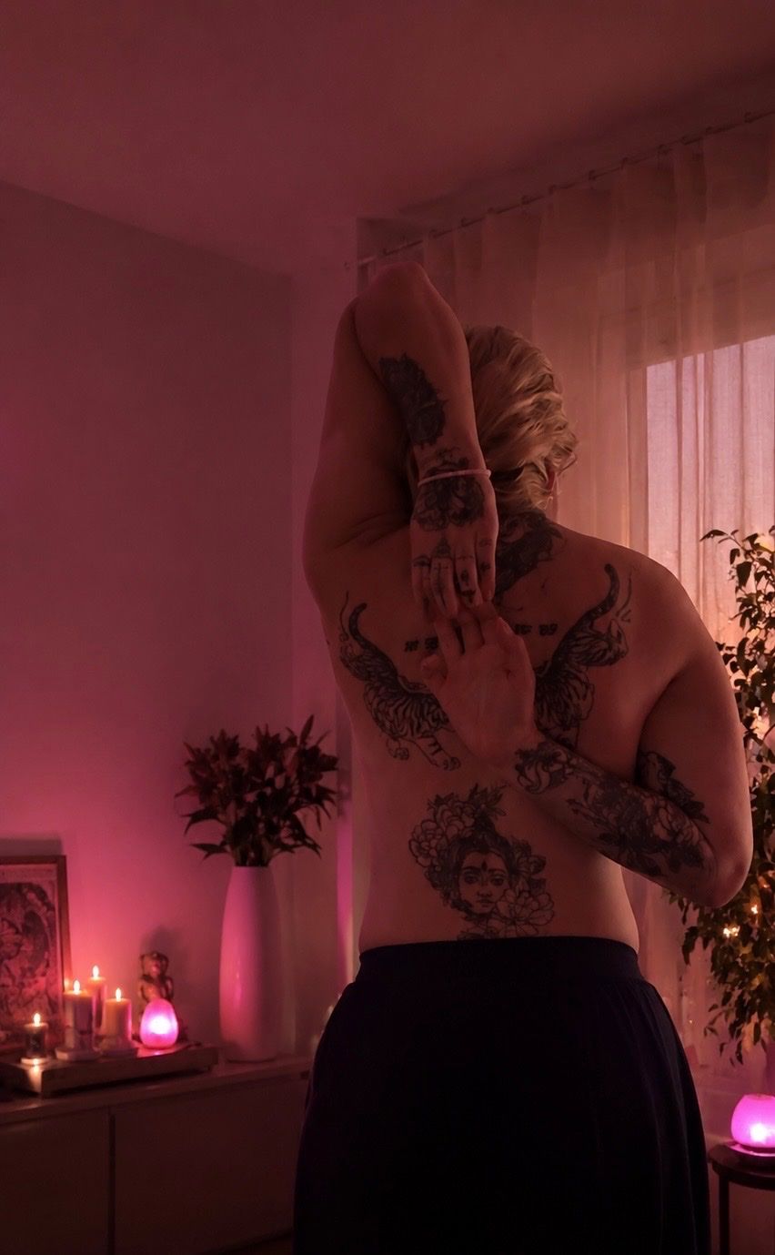 Diana, the masseuse, seen from behind stretching her arms in a room with candles and pink light